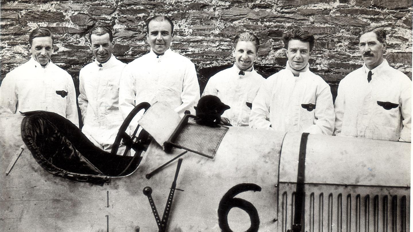 Six of the Bentley Boys stood by a racing Bentley in a group photograph