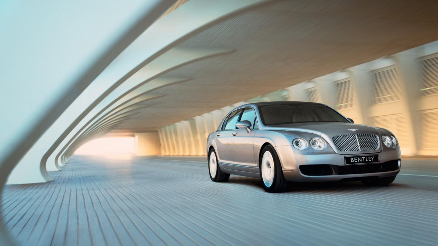 A front three quarter launch image of the Continental Flying Spur driving under a contemporary bridge