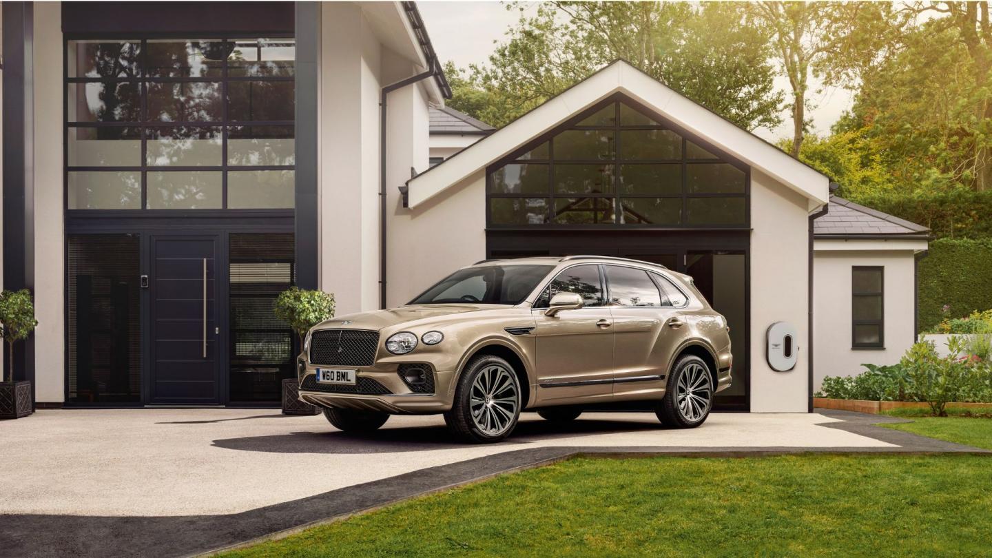 The second generation of Bentayga parked outside a modern rural family home being charged via wall charger