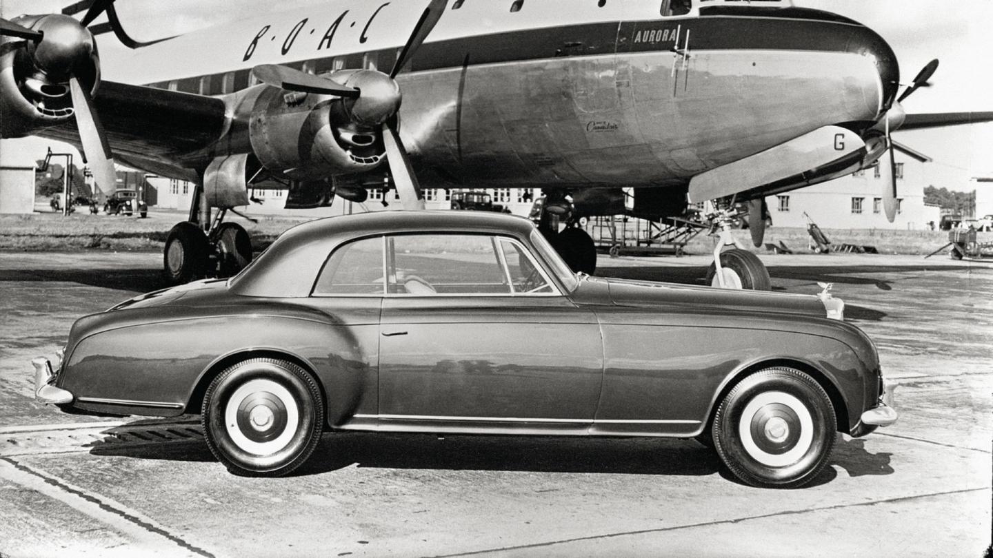 A side profile image of a Bentley S1 parked alongside a rotary aeroplane