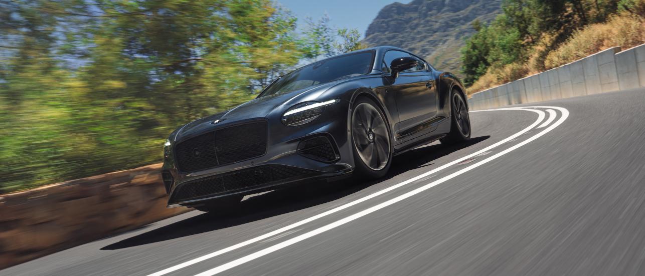 The new Hybrid Bentley Continental GT S in Thunder Grey driving dynamically in a rural environment