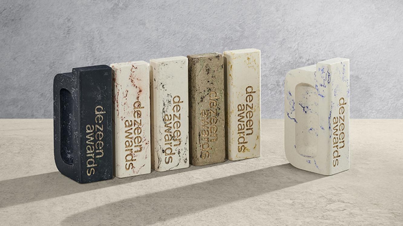 Six abstract patterned trophies made from London Clay featuring Dezeen awards engraving, placed on marble surface.