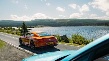 Rear view of Bentley Continental GT in Orange Flame Colour driving along a lake.