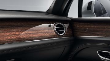 Bentley Bentayga EWB passenger side view overlooking Chrome metal bulls-eye air vents set in Crown Cut Walnut veneer.