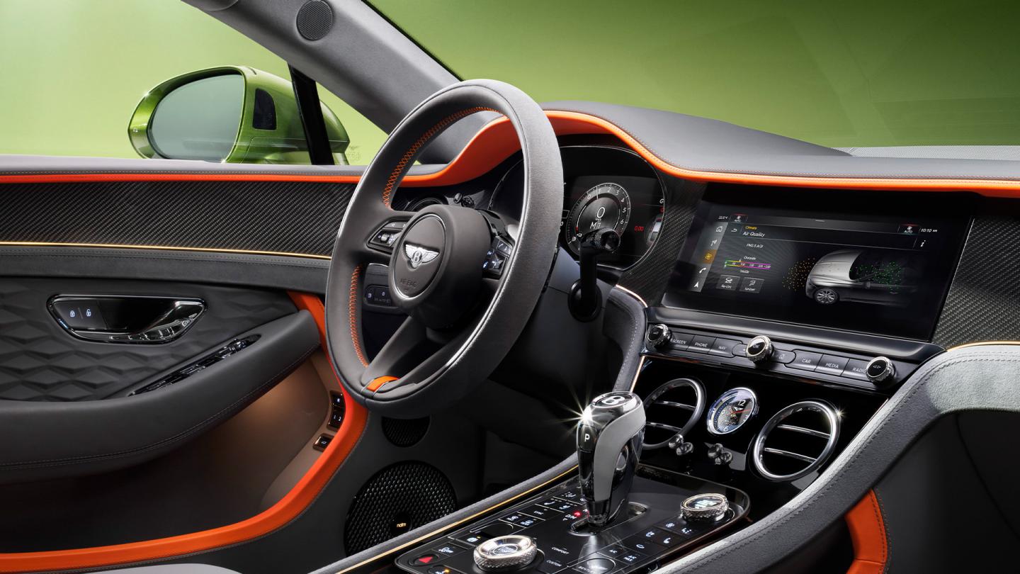Driver side view of new Bentley Continental GT Speed with steering wheel in view featuring High Gloss Carbon Fibre veneer and Mandarin by Mulliner hide.