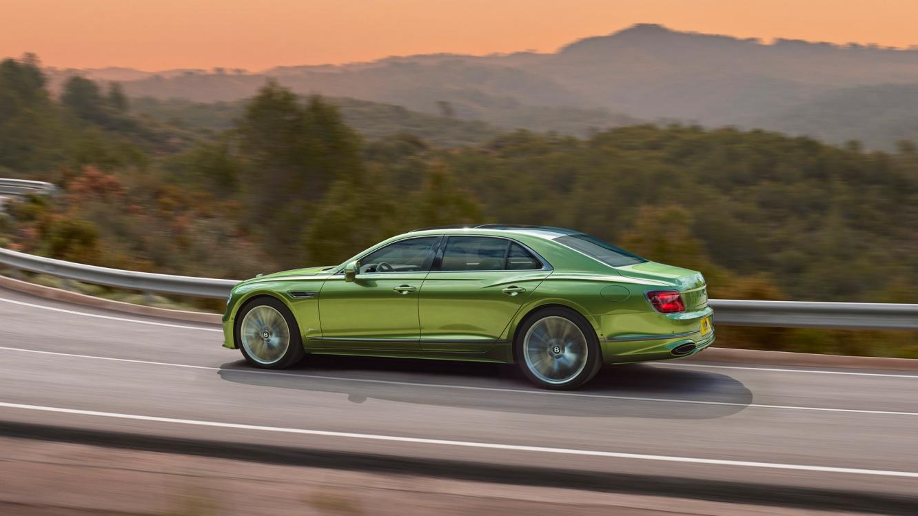 Rear 3/4 of new Bentley Flying Spur speed in Tourmaline Green featuring Flying ‘B’ radiator mascot – bright polished stainless, driving along a bridge in the mountains